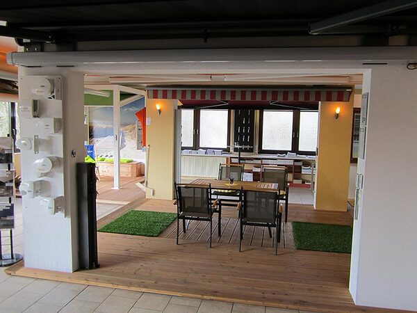 Überdachte Terrasse mit Markise, Holzboden, Gartenmöbeln und modernem Wintergarten.